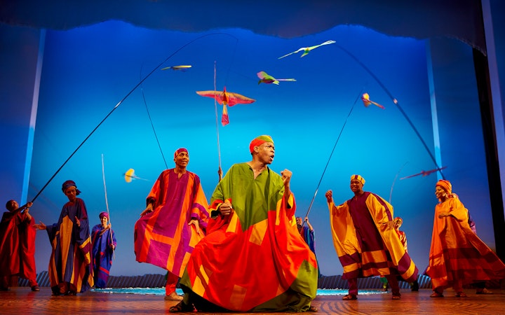 Performers in colorful costumes on stage during The Lion King musical.