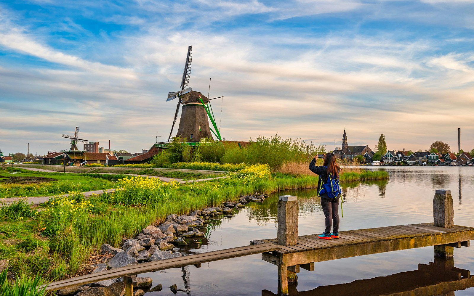 Dutch windmill at Zaanse Schans Village with visitor taking photo by the water.