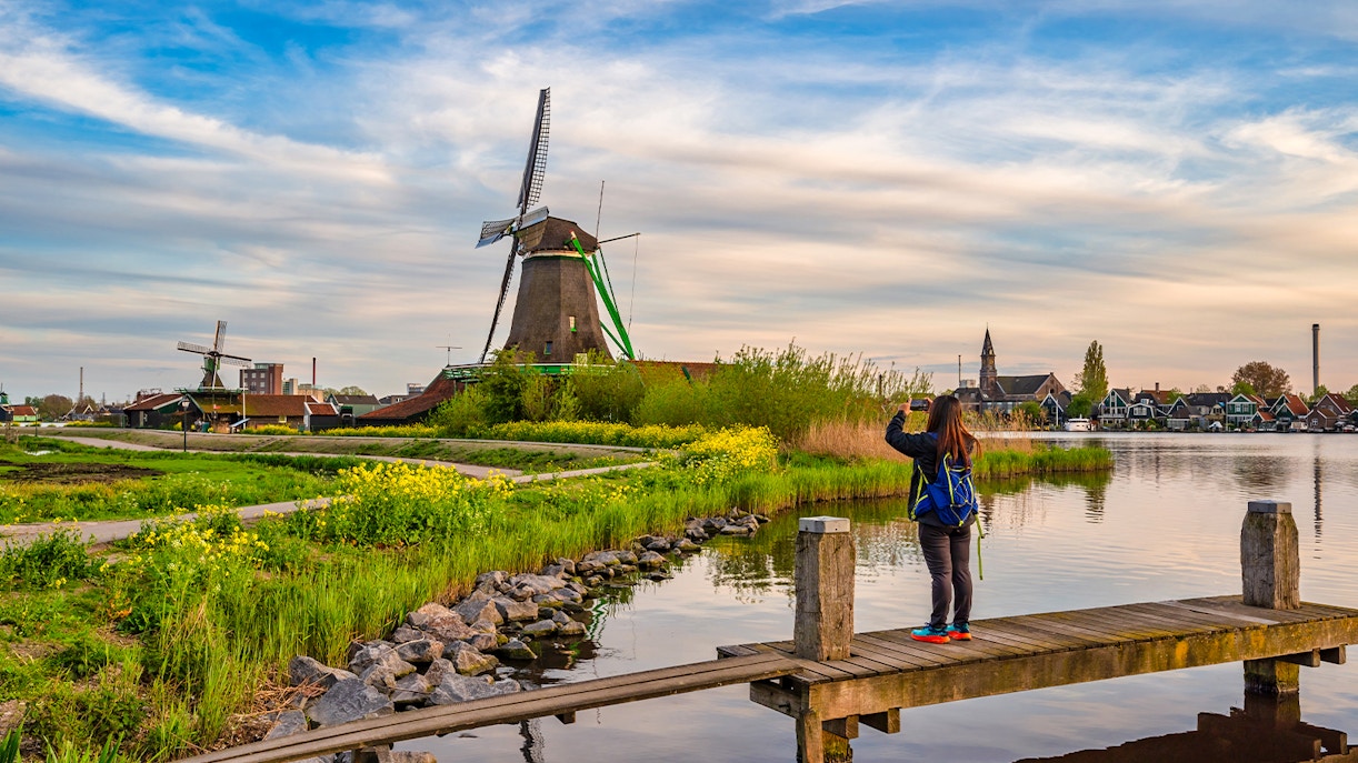 Dutch windmill at Zaanse Schans Village with visitor taking photo by the water.