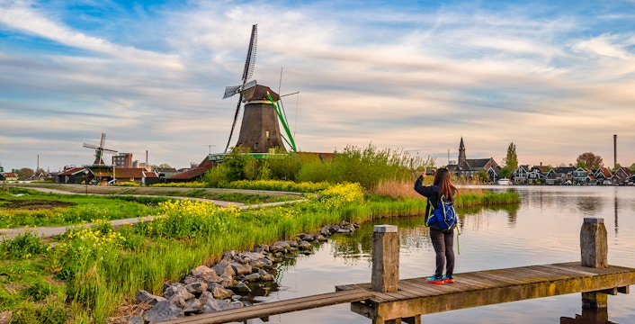 Dutch windmill at Zaanse Schans Village with visitor taking photo by the water.