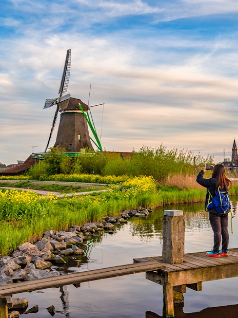 Dutch windmill at Zaanse Schans Village with visitor taking photo by the water.