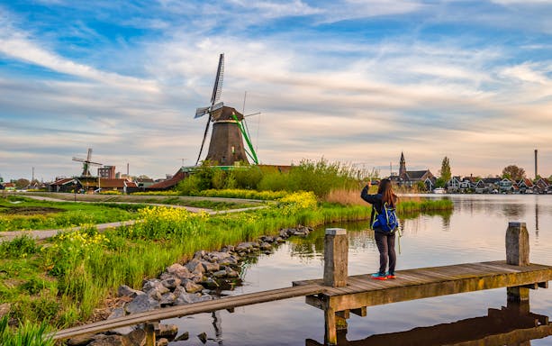 Dutch windmill at Zaanse Schans Village with visitor taking photo by the water.