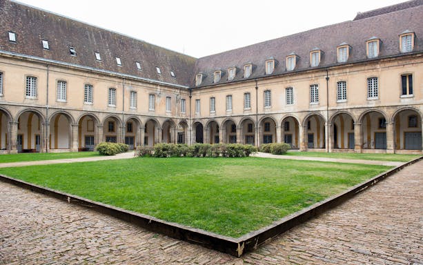 Abbaye de Cluny courtyard with arched walkways and green lawn in France.