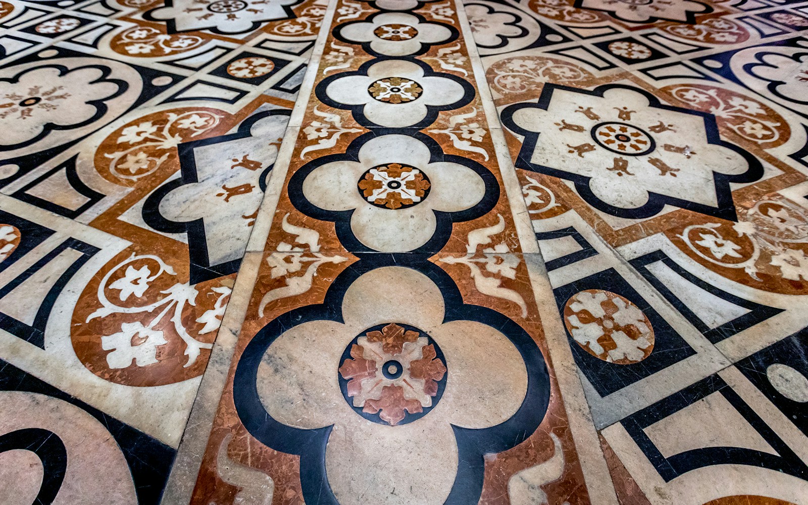 Intricate geometric and floral patterns on the marble flooring inside Duomo Milan Cathedral.
