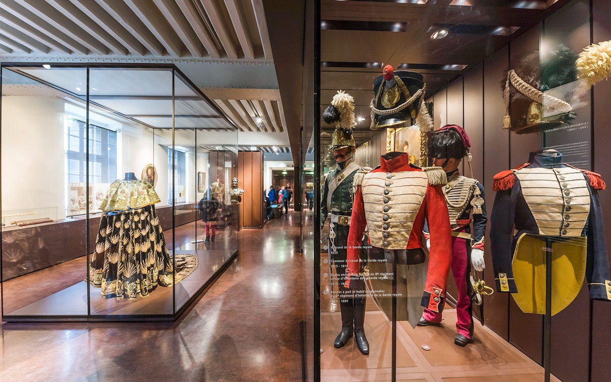 Armour suits and uniforms displayed at Army Museum, Paris with visitors exploring exhibits.