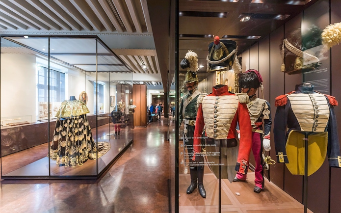Armour suits and uniforms displayed at Army Museum, Paris with visitors exploring exhibits.