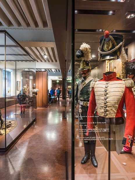 Armour suits and uniforms displayed at Army Museum, Paris with visitors exploring exhibits.