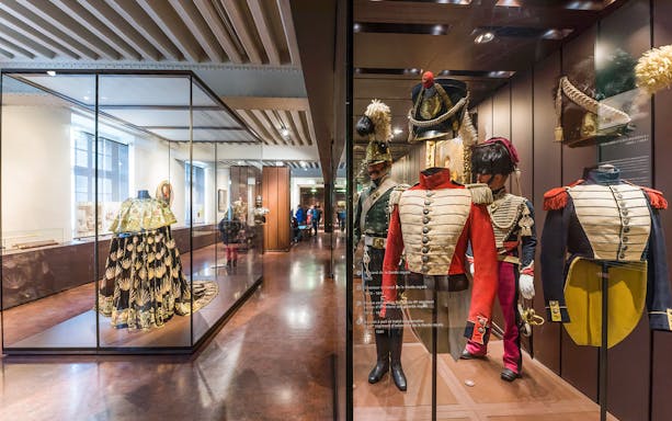 Armour suits and uniforms displayed at Army Museum, Paris with visitors exploring exhibits.