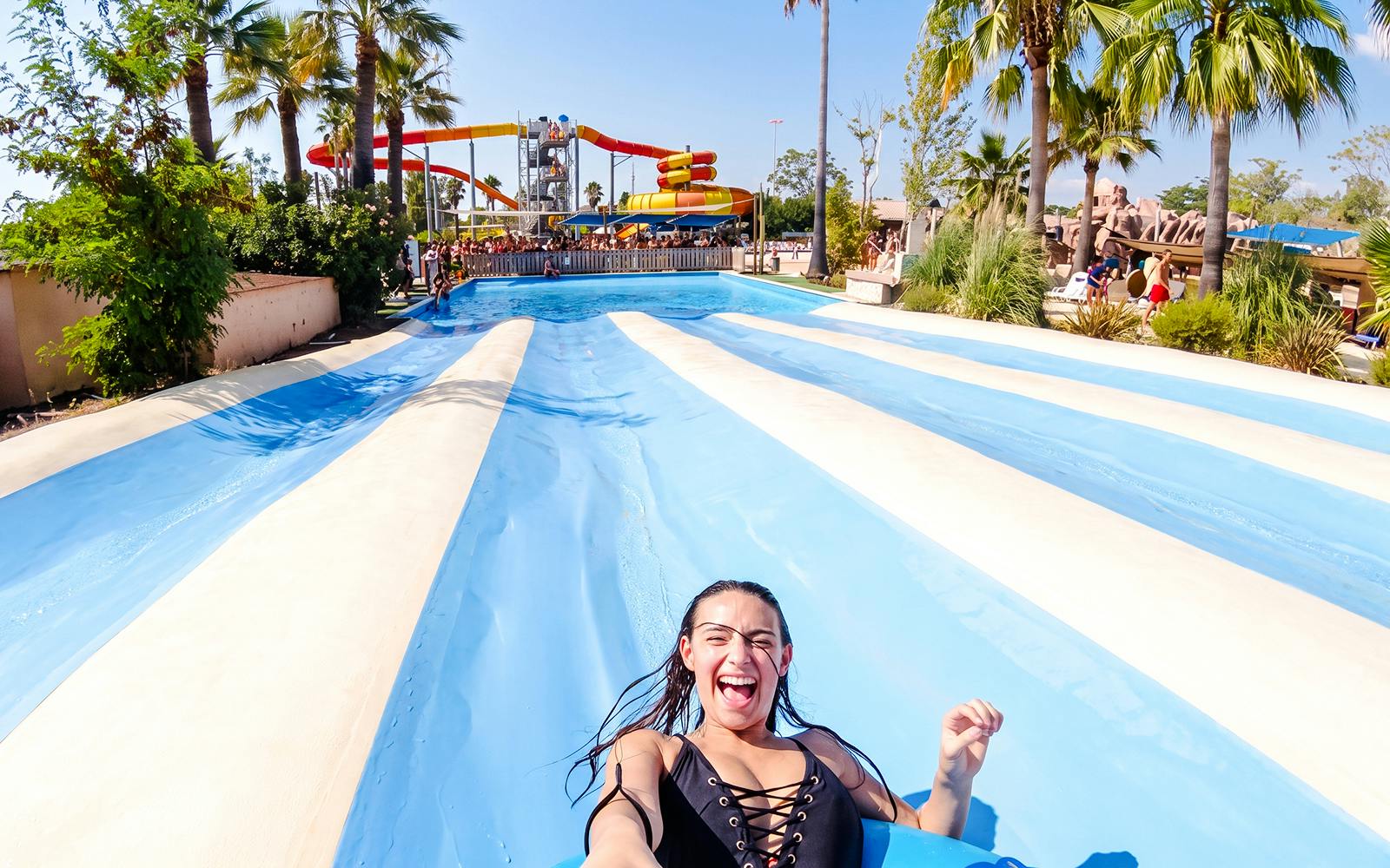 Person enjoying a water slide at Aquasplash Antibes with palm trees and slides in the background.