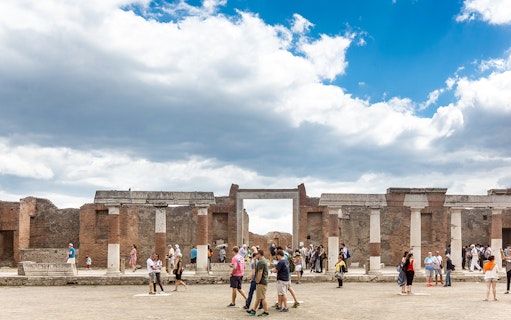 Tourists exploring ancient ruins in Pompeii, Italy, under a cloudy sky.