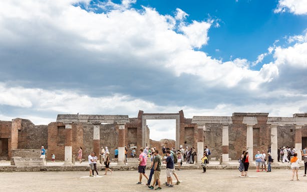 Tourists exploring ancient ruins in Pompeii, Italy, under a cloudy sky.