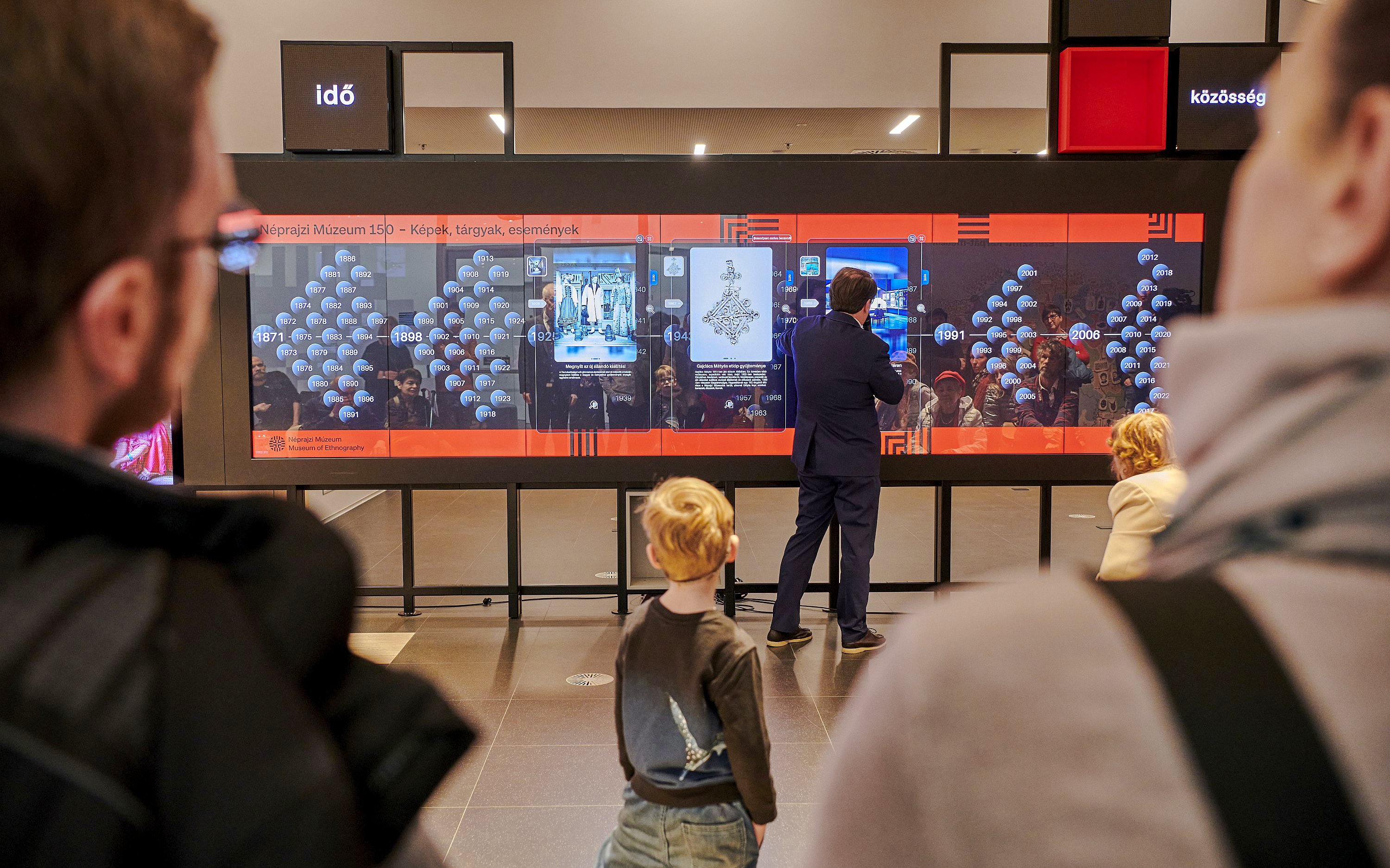 Interactive exhibit at Museum of Ethnography, Budapest, with visitors observing a digital timeline display.