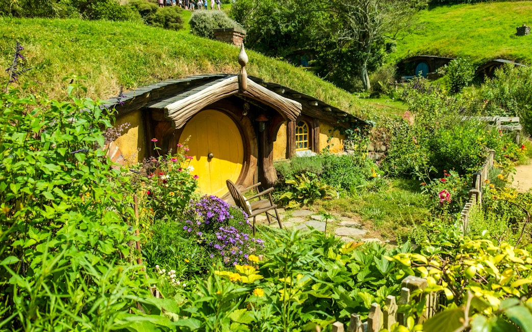 Yellow door hobbit house surrounded by lush greenery at Hobbiton movie set.