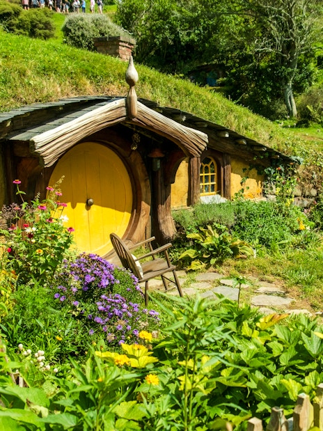Yellow door hobbit house surrounded by lush greenery at Hobbiton movie set.