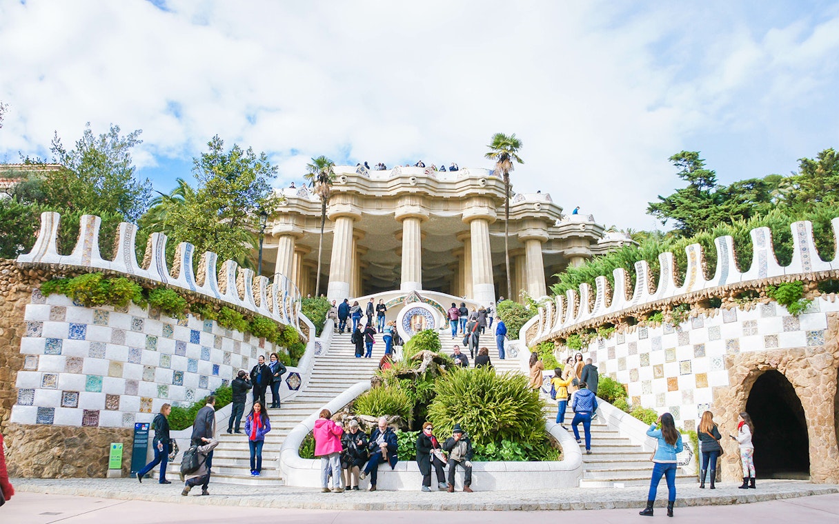 Park Güell entrance with mosaic walls and visitors in Barcelona.