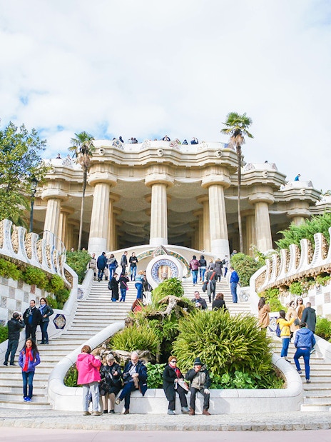 Park Güell entrance with mosaic walls and visitors in Barcelona.