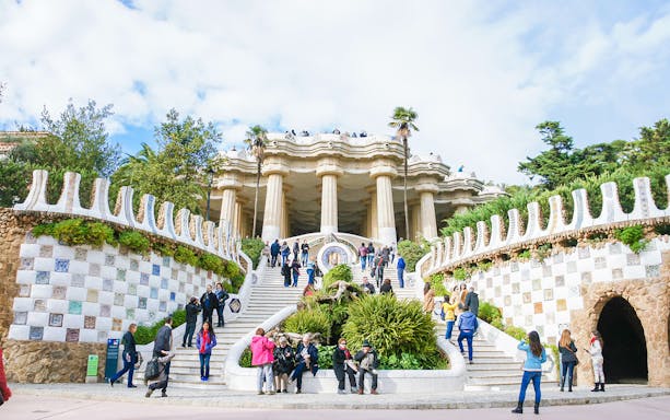 Park Güell entrance with mosaic walls and visitors in Barcelona.