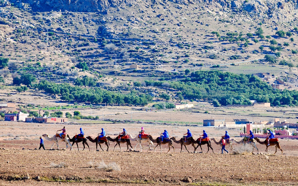 Tourists riding camels in Agafay Desert, Marrakesh with rocky landscape in background.