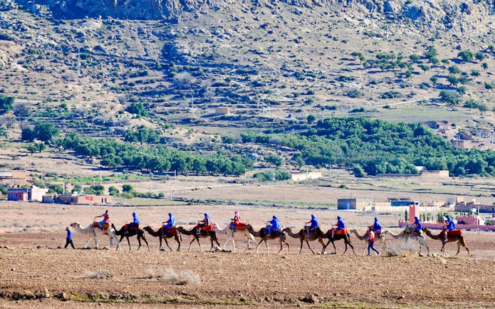Tourists riding camels in Agafay Desert, Marrakesh with rocky landscape in background.