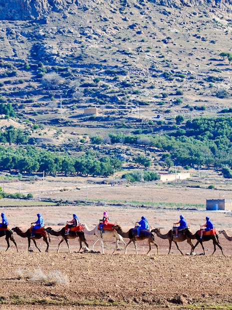 Tourists riding camels in Agafay Desert, Marrakesh with rocky landscape in background.