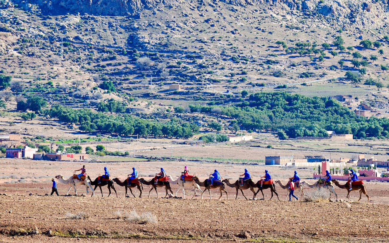 Tourists riding camels in Agafay Desert, Marrakesh with rocky landscape in background.