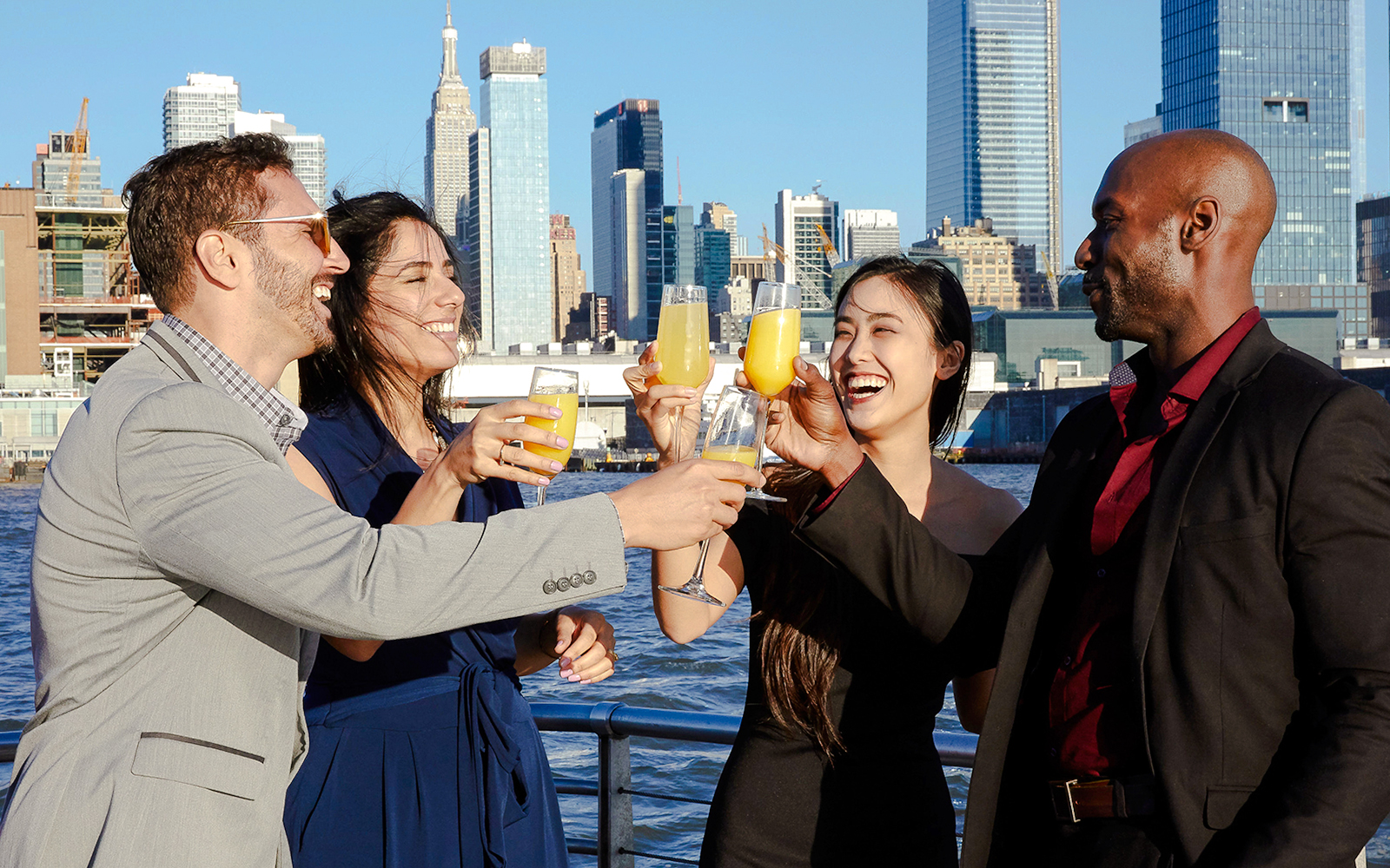 Group toasting with drinks on New Jersey Signature Cruise with city skyline in background.