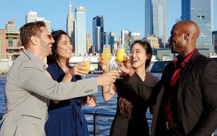 Group toasting with drinks on New Jersey Signature Cruise with city skyline in background.