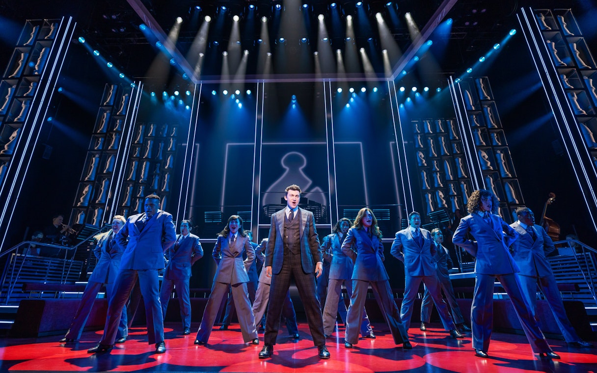 Stage performance of Chess Broadway show with cast in suits under blue lighting.