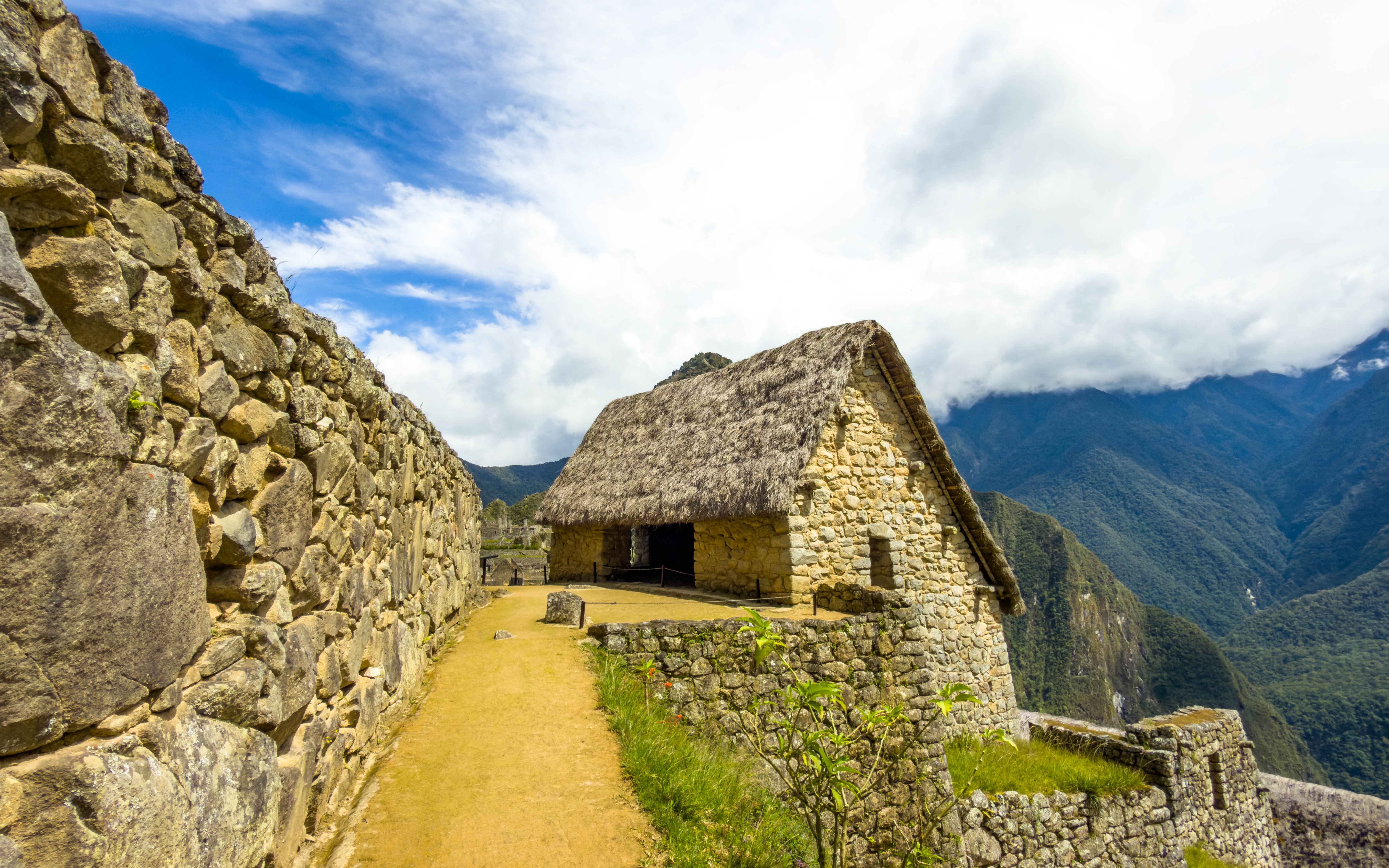 Stone house with thatched roof at Machu Picchu, Peru, with mountain backdrop.
