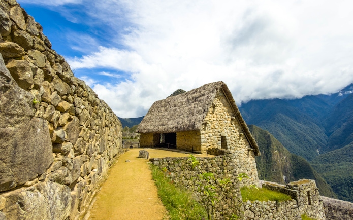 Stone house with thatched roof at Machu Picchu, Peru, with mountain backdrop.