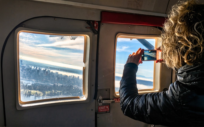 Woman photographing Vancouver skyline from seaplane window on Scenic Panorama Tour.