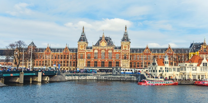 Amsterdam Centraal Station with canal and boats in foreground.