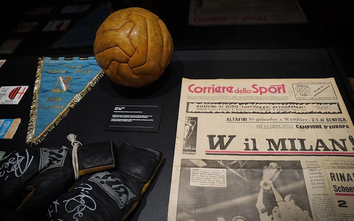 Vintage football memorabilia at Casa Milan Museum, Italy, featuring a leather ball, newspaper, and pennant.