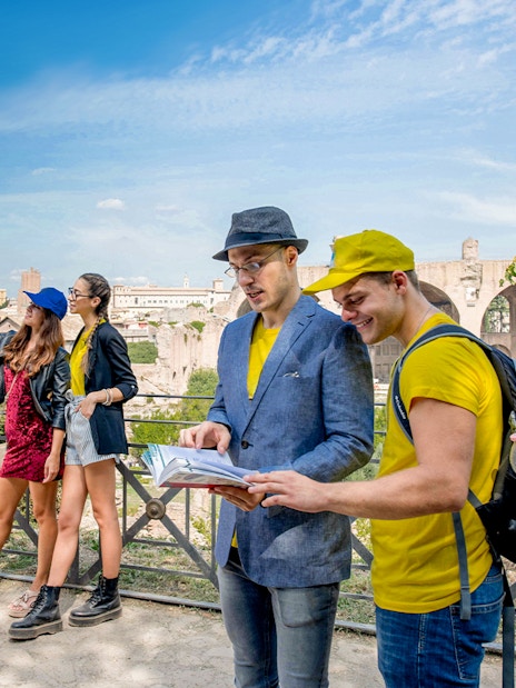 Tourists exploring the Roman Forum with a guidebook, Colosseum in the background.