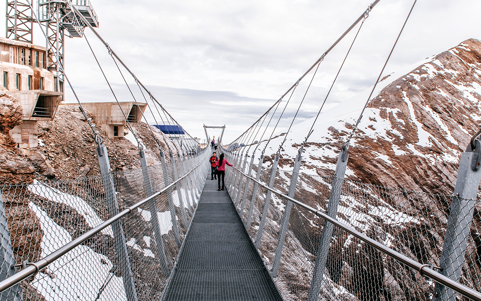 Visitors on Cliff Walk bridge at Titlis, surrounded by snowy mountains.
