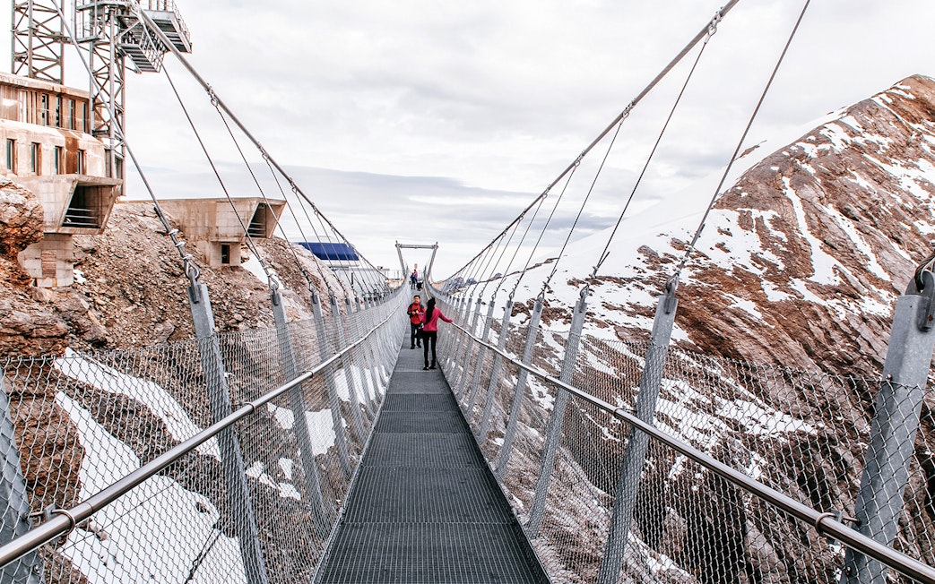 Visitors on Cliff Walk bridge at Titlis, surrounded by snowy mountains.