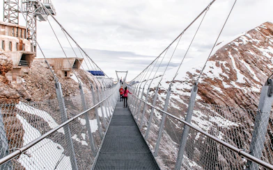 Visitors on Cliff Walk bridge at Titlis, surrounded by snowy mountains.