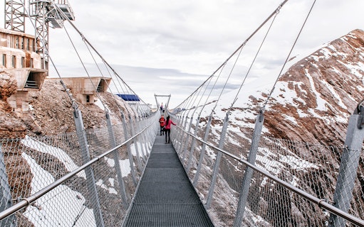 Visitors on Cliff Walk bridge at Titlis, surrounded by snowy mountains.
