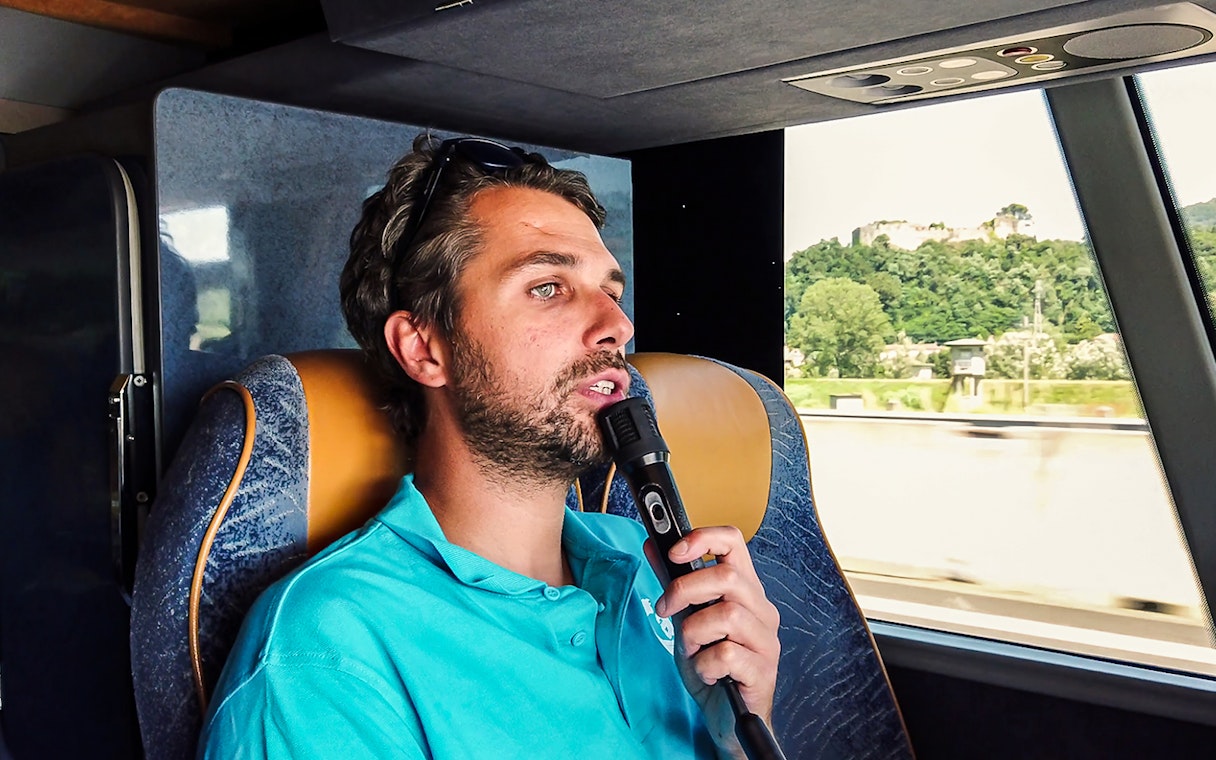 Tour guide speaking into a microphone on a bus during a guided tour from Florence to Pisa.