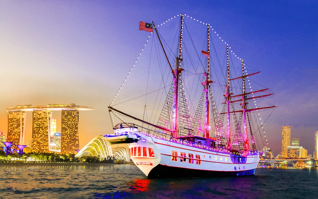 Sailing ship Royal Albatross illuminated at night with Singapore skyline in the background.