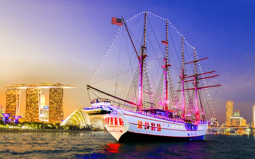 Sailing ship Royal Albatross illuminated at night with Singapore skyline in the background.