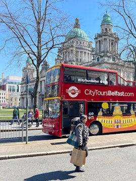 Red double-decker bus in front of Belfast City Hall on a sunny day.