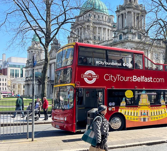 Red double-decker bus in front of Belfast City Hall on a sunny day.