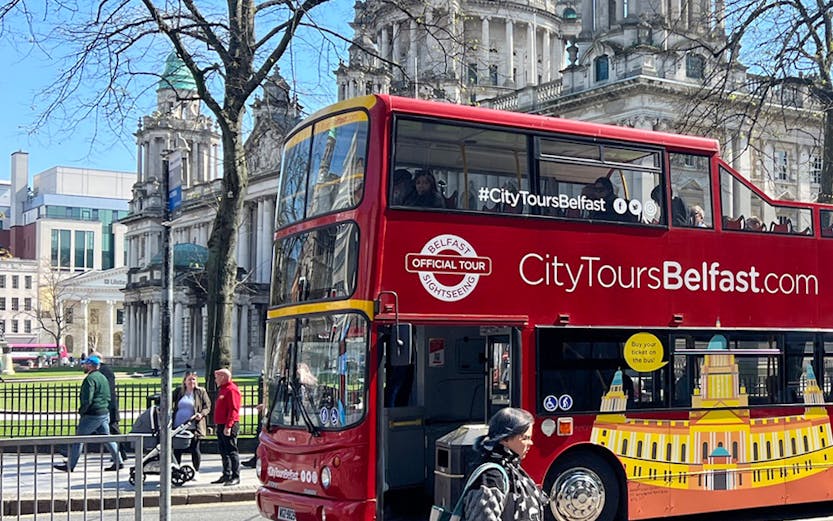 Red double-decker bus in front of Belfast City Hall on a sunny day.