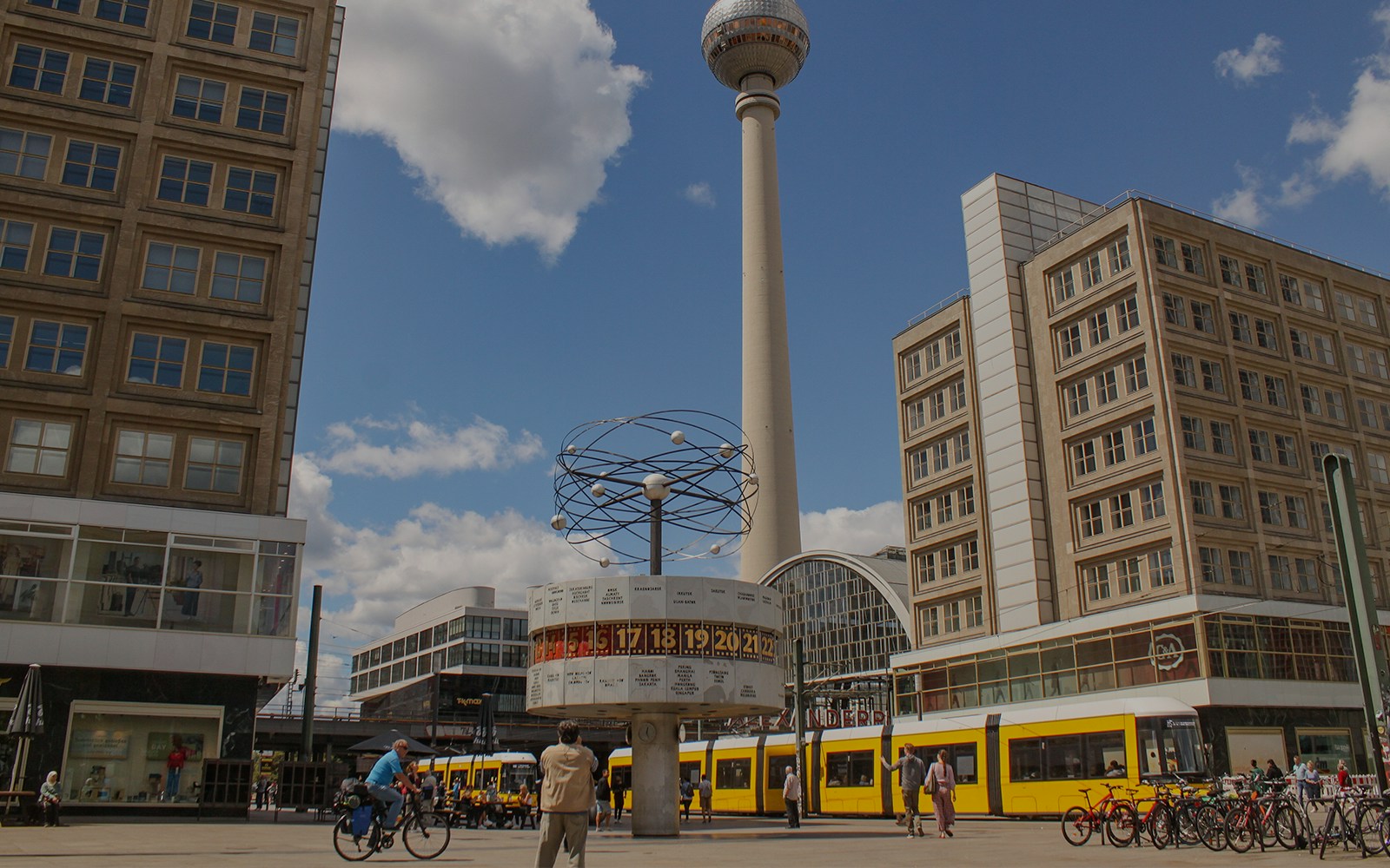 World clock and TV tower at Alexanderplatz, Berlin with tram and cyclists nearby.