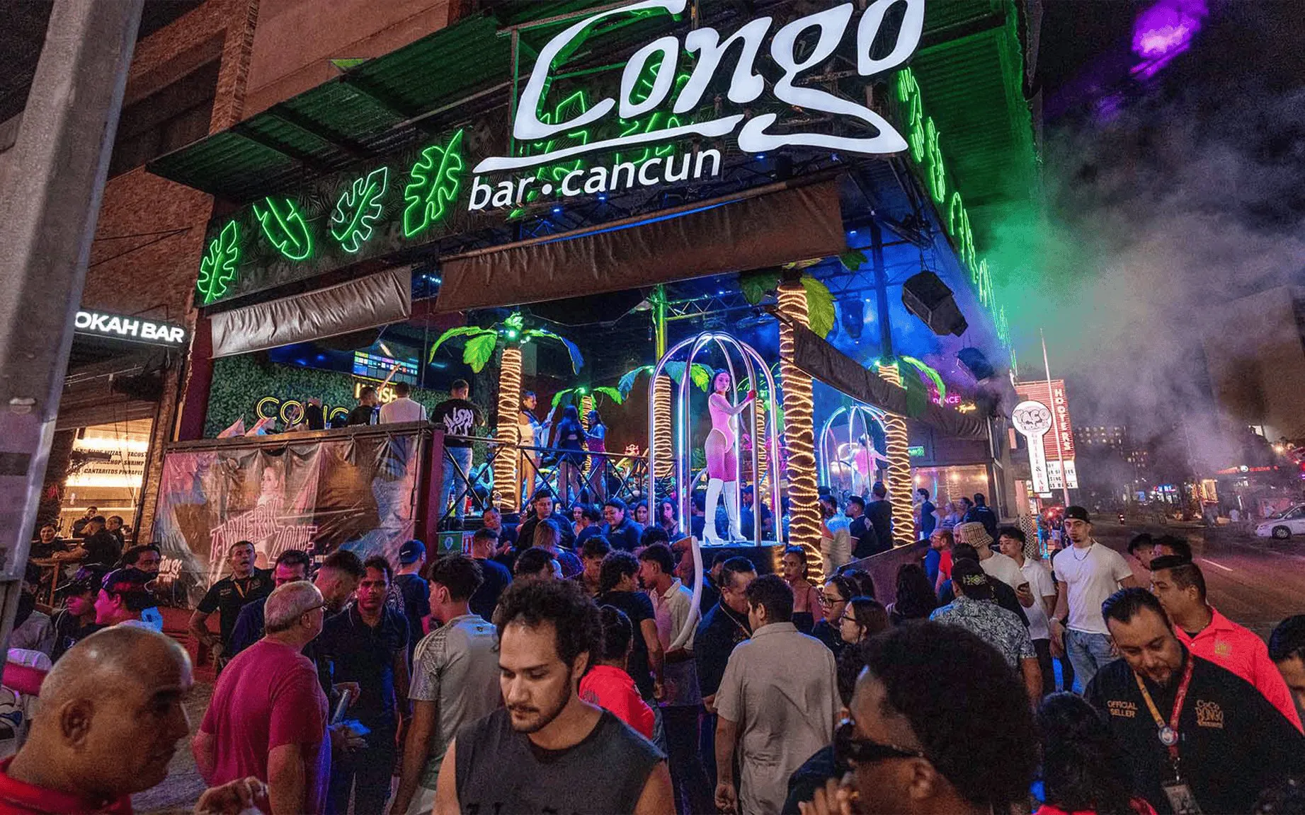 Crowd outside Coco Bongo Congo Bar in Cancun at night with neon lights and palm decorations.