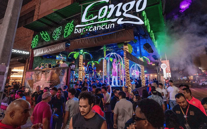 Crowd outside Coco Bongo Congo Bar in Cancun at night with neon lights and palm decorations.