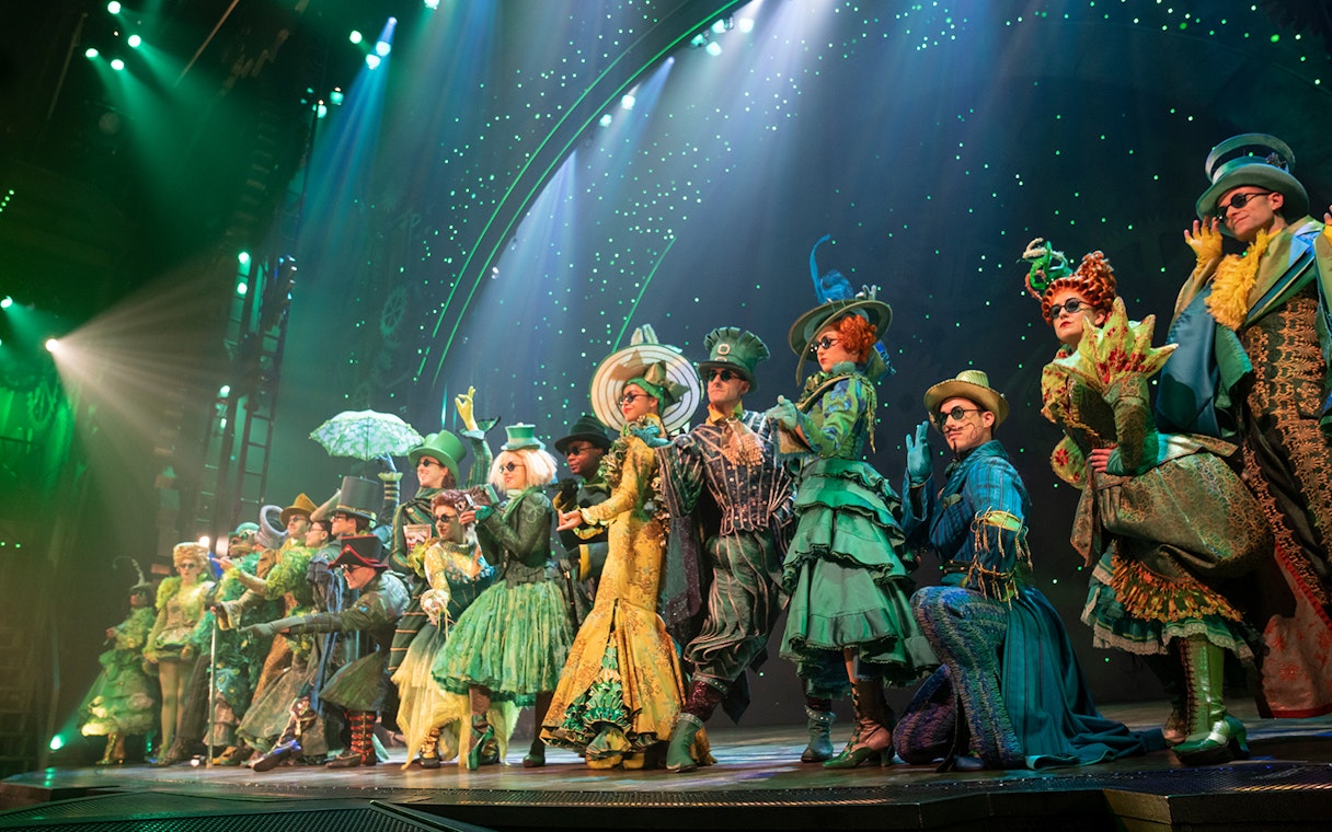 Performers in elaborate green costumes on stage during a scene from Wicked musical.