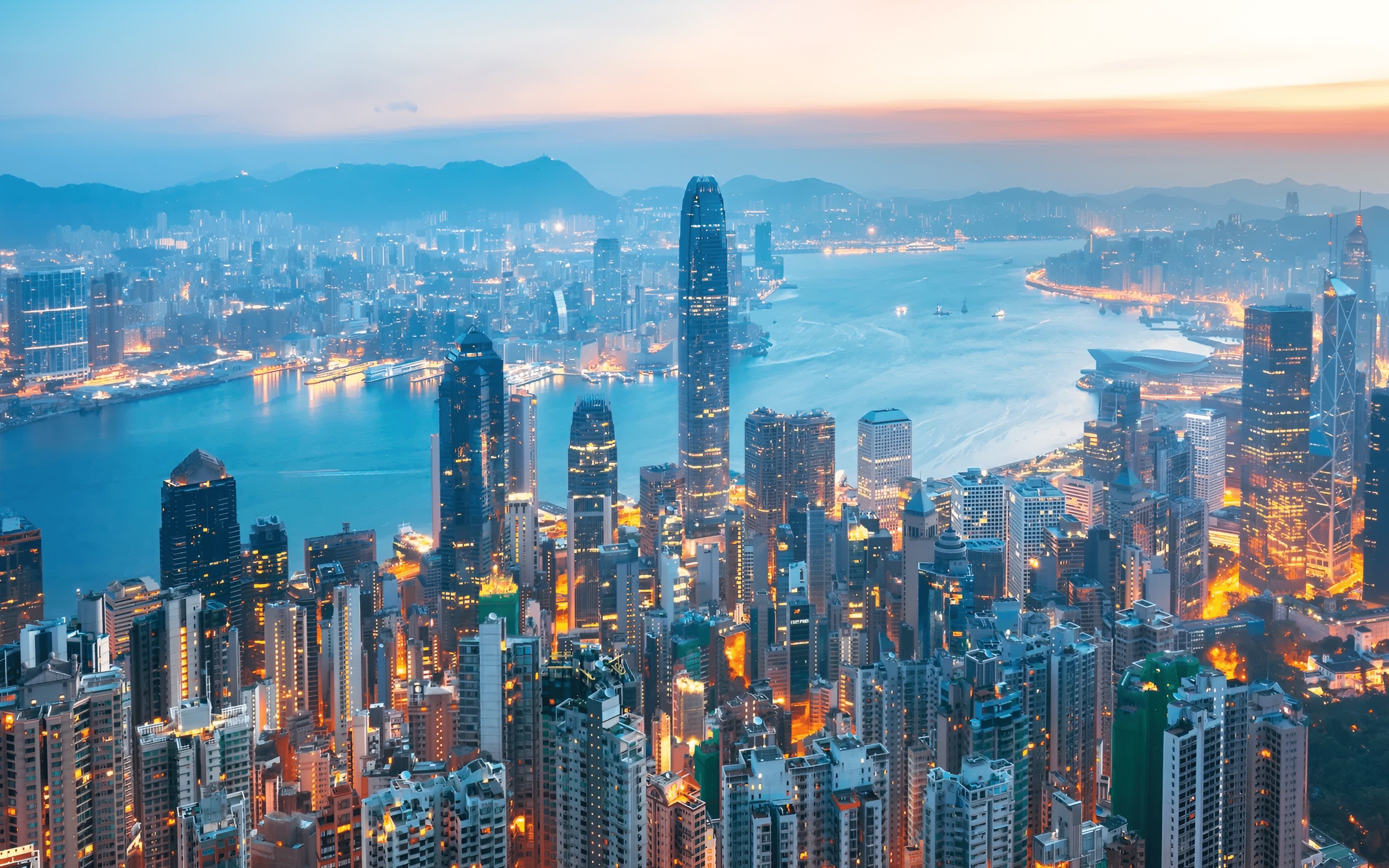Aerial view of Hong Kong Island skyline at dusk with illuminated skyscrapers and Victoria Harbour.