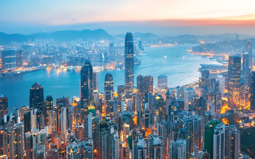 Aerial view of Hong Kong Island skyline at dusk with illuminated skyscrapers and Victoria Harbour.